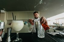 Camarero vertiendo bebidas alcohólicas a agitador en el bar - foto de stock