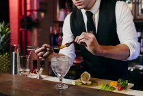 Ritaglia anonimo giovane elegante barman che lavora dietro un bancone del bar mescolando bevande con frutta — Foto stock