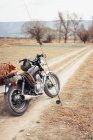 Fishing pole and motorcycle located on narrow countryside road in dry field during trip in nature — Stock Photo
