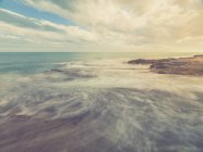 Скелястий берег і блакитні моря пінний на тлі неба з хмарами — стокове фото