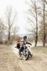 Masculino no capacete equitação rápido moto no empoeirado campo estrada perto de folhosas árvores no natureza — Fotografia de Stock