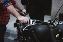 Культурист тримає чорний мотоцикл, припаркований на асфальті на міській вулиці — стокове фото