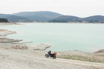 Motocicleta estacionada na estrada rural na costa do lago tranquilo durante a viagem na natureza — Fotografia de Stock