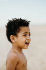 Seitenansicht des entzückenden, hemdlosen afroamerikanischen Jungen, der wegschaut, während er auf verschwommenem Strand-Hintergrund steht — Stockfoto