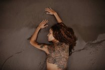 Mulher nua com costas tatuadas e ombro deitado na areia molhada na praia — Fotografia de Stock