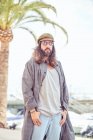 Stylish bearded man with long hair walking on street with sunglasses near palm tree — Stock Photo