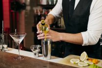 Ritaglia anonimo giovane elegante barman che lavora dietro un bancone del bar mescolando bevande con frutta — Foto stock