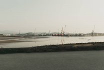 Paisaje industrial con bahía marítima y grúas portuarias en terreno montañoso en día nublado - foto de stock