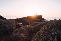 Homme randonneur prendre des photos tout en marchant sur le bord de mer au coucher du soleil — Photo de stock