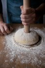 Cocinero masculino irreconocible dando forma a masa fresca con harina mientras cocina Rosca de Reyes sobre mesa de madera en la cocina . - foto de stock