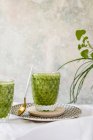 Frullato verde sano di spinaci, avocado e kiwi, mela e limone in bicchieri su piatto fantasia — Foto stock