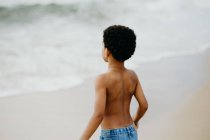 Funny African American boy playing on sandy shore near sea — Stock Photo