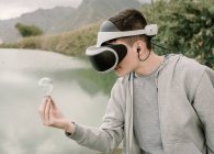 Jovem adolescente jogando uma simulação de realidade virtual com óculos VR em pé perto de um lago segurando uma lâmpada iinovação e conceito de energia — Fotografia de Stock