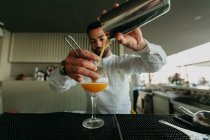 Bartender pouring cocktail from shaker in glass in bar — Stock Photo