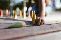 Unrecognizable shirtless African American boy sitting on wooden surface and playing with colorful cones on sunny day — Stock Photo