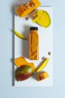 Smoothie végétalien à la mangue et à la citrouille en bouteille sur tableau blanc avec ingrédients — Photo de stock