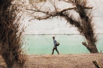 Вид збоку чоловіка з рюкзаком, що стоїть на березі озера та рибалить у сонячний день у природі — стокове фото