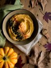 Conjunto de delicioso hummus de calabaza con semillas en una servilleta de tela colocada sobre una mesa de madera con hojas secas de otoño. - foto de stock