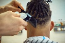 Vue de la récolte de derrière du coiffeur anonyme faisant une coupe de cheveux moderne avec un rasoir à un client afro-américain sans visage — Photo de stock