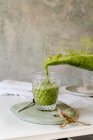 Serving homemade healthy green smoothie of spinach, avocado and kiwi, apple and lemon in glass on wooden board — Stock Photo