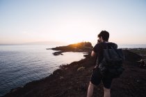 Fotógrafo masculino retratando o pôr do sol acima da costa remota — Fotografia de Stock