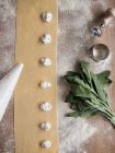 Hands of anonymous cook squeezing creamy filling on thin ravioli dough near bunch of fresh sorrel on table in kitchen — Stock Photo