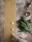 Mains de cuisinier anonyme serrant remplissage crémeux sur la pâte de raviolis mince près du bouquet d'oseille fraîche sur la table dans la cuisine — Photo de stock