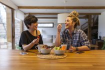 Duas mulheres bonitas e jovens tomando café da manhã em casa e se divertindo — Fotografia de Stock
