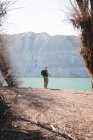 Vista posteriore del maschio con zaino in piedi sulla riva del lago e la pesca nella giornata di sole nella natura — Foto stock