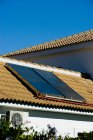 Casa de campo suburbana com painéis solares instalados no telhado de azulejos contra céu azul sem nuvens — Fotografia de Stock