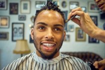 Анонімний перукар робить сучасну стрижку веселому афроамериканському клієнту — стокове фото
