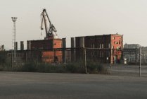 Old functioning red brick factory buildings, pipes and crane placing on industrial area behind fence — Stock Photo