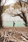 Vista lateral do macho com mochila em pé na costa do lago e pesca no dia ensolarado na natureza — Fotografia de Stock
