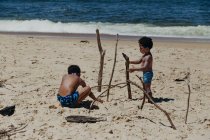 Deux frères afro-américains avec des bâtons jouant ensemble sur le rivage sablonneux près de la mer — Photo de stock