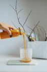 Female hand serving fresh mango smoothie into glass on white table — Stock Photo