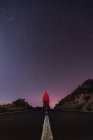 Viajante com capuz vermelho jaqueta de pé na estrada vazia à noite — Fotografia de Stock