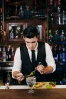 Joven barman elegante que trabaja detrás de un mostrador de bar mezclando bebidas con frutas - foto de stock