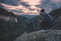 Uomo con macchina fotografica seduto sulla montagna collina con magnifico tramonto — Foto stock