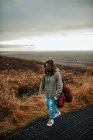 Junge Wanderin in Komfortkleidung mit Rucksack wandert durch Wüstenlandschaft vor grauem, düsterem Himmel — Stockfoto