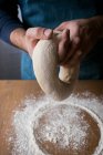 Неузнаваемый мужчина готовит свежее тесто с мукой, пока готовит Рошку де Рейес над деревянным столом на кухне. . — стоковое фото