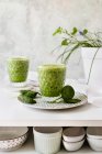 Healthy green smoothie of spinach, avocado and kiwi, apple and lemon in glasses on patterned plate — Stock Photo
