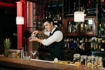Young elegant barman working behind a bar counter mixing drinks in a shaker — Stock Photo
