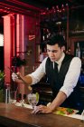 Giovane elegante barman che lavora dietro un bancone del bar mescolando bevande con frutta — Foto stock