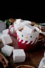 Ароматические палочки корицы и сушеные цитрусовые, помещенные на пилораме возле чашек вкусного горячего шоколада с мягкими зефирами и различными рождественскими украшениями — стоковое фото