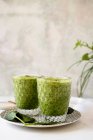 Batido verde saludable de espinacas, aguacate y kiwi, manzana y limón en vasos en plato estampado - foto de stock