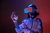 Возбужденная молодая женщина касается воздуха, испытывая опыт виртуальной реальности в неоновом свете — стоковое фото