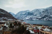 Erstaunlicher Drohnenblick auf kleine Siedlung in der Nähe des ruhigen Meeres und des wunderschönen schneebedeckten Bergrückens an bewölkten Tagen — Stockfoto