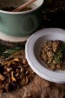 Pan y plato de delicioso risotto de arroz con carne de conejo y champiñones decorados con ramita de romero fresco en la cocina - foto de stock