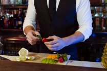 Crop anonimo giovane elegante barman che lavora dietro un bancone del bar preparare frutta per cocktail bevande — Foto stock