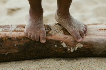 Брудні ноги невпізнаваної чорної дитини, що ходить по колоді на піщаному пляжі — стокове фото